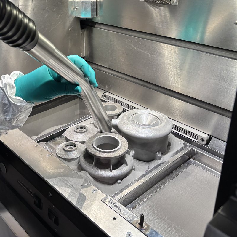 Gloved hands depowdering printed parts in the build chamber