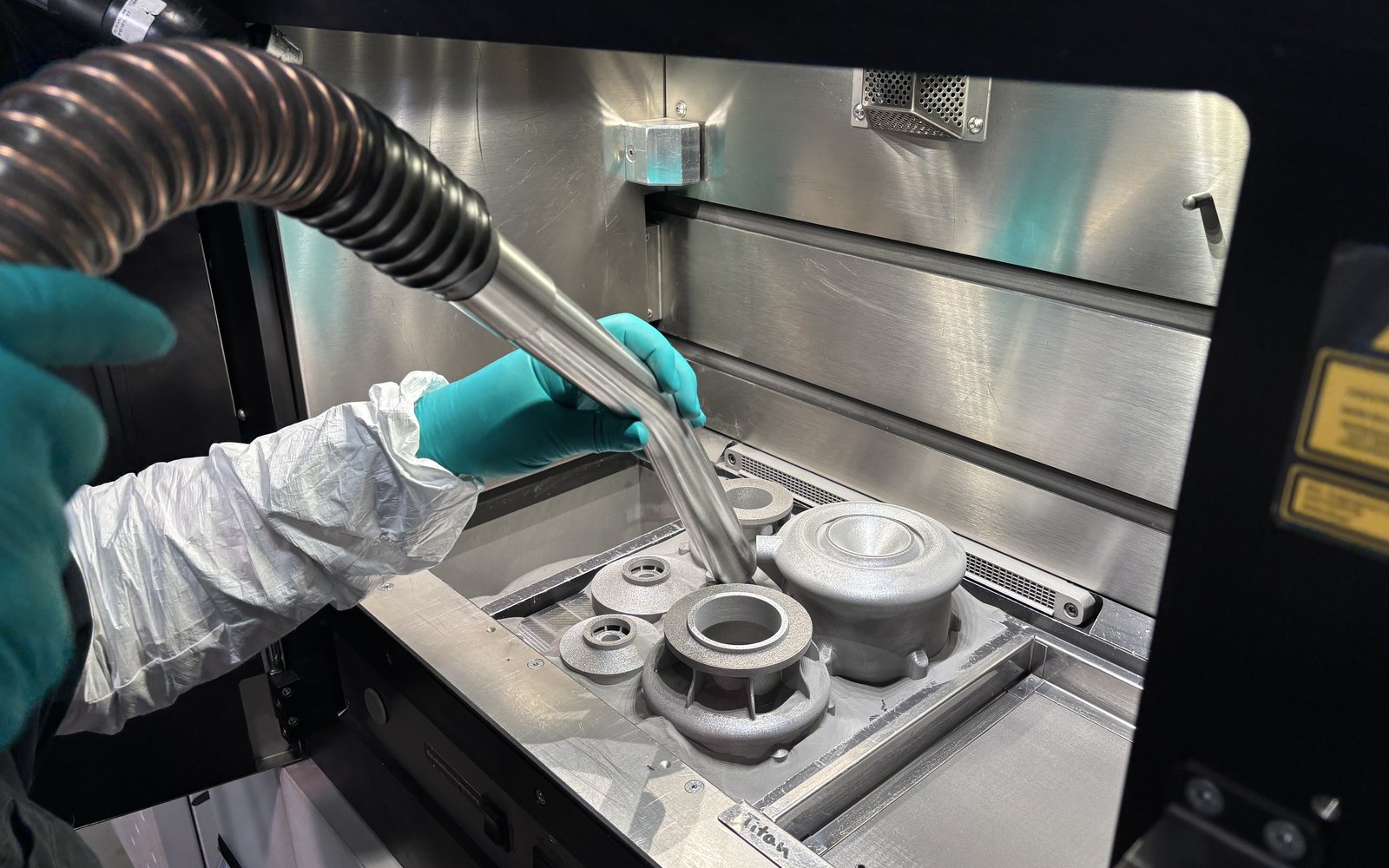 Gloved hands depowdering freshly printed metal parts inside an LPBF machine